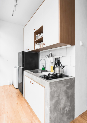 The photo shows the kitchenette of color along with the refrigerator of black color and hanging cabinets